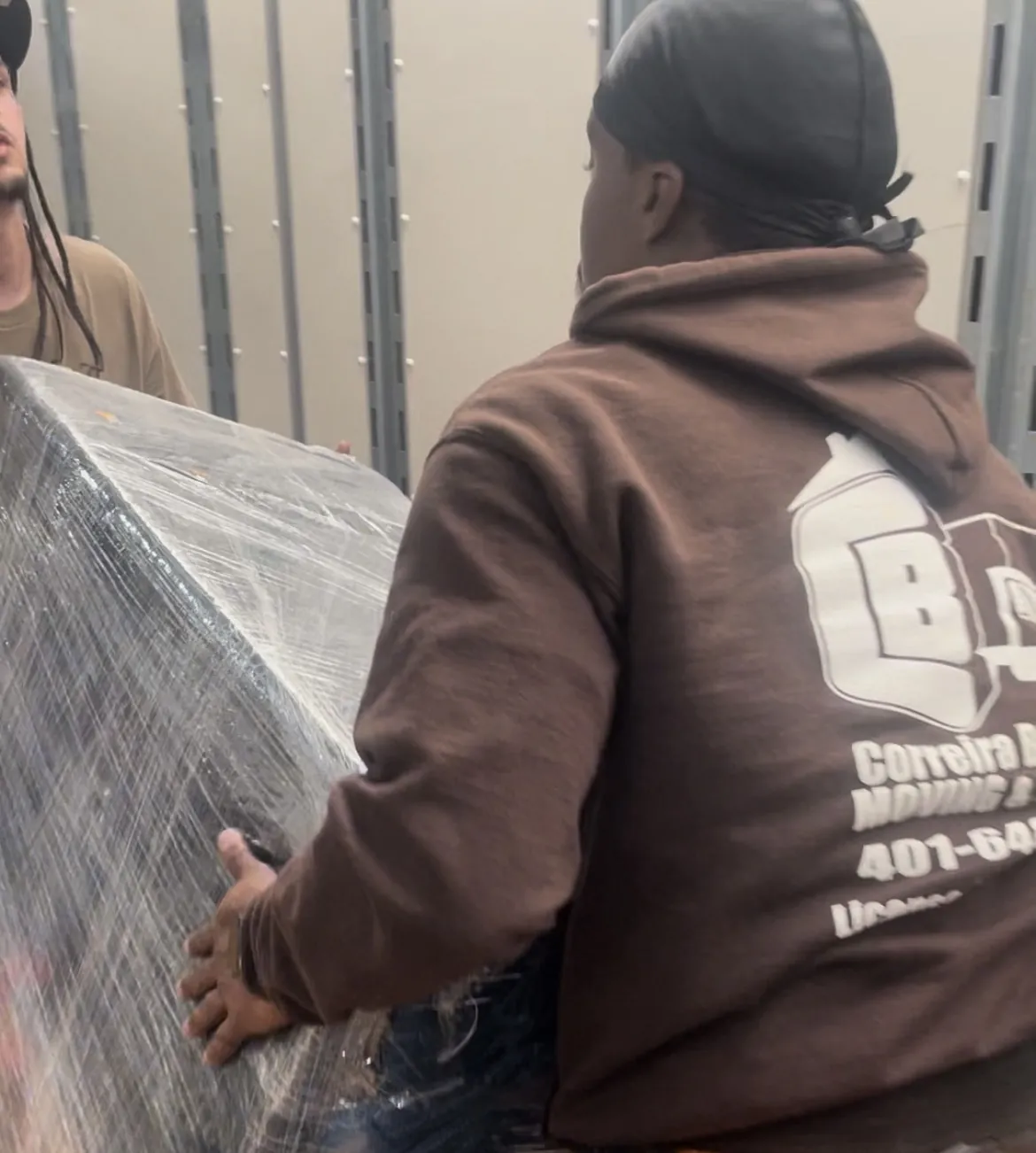 Mover in company hoodie carrying a wrapped item indoors