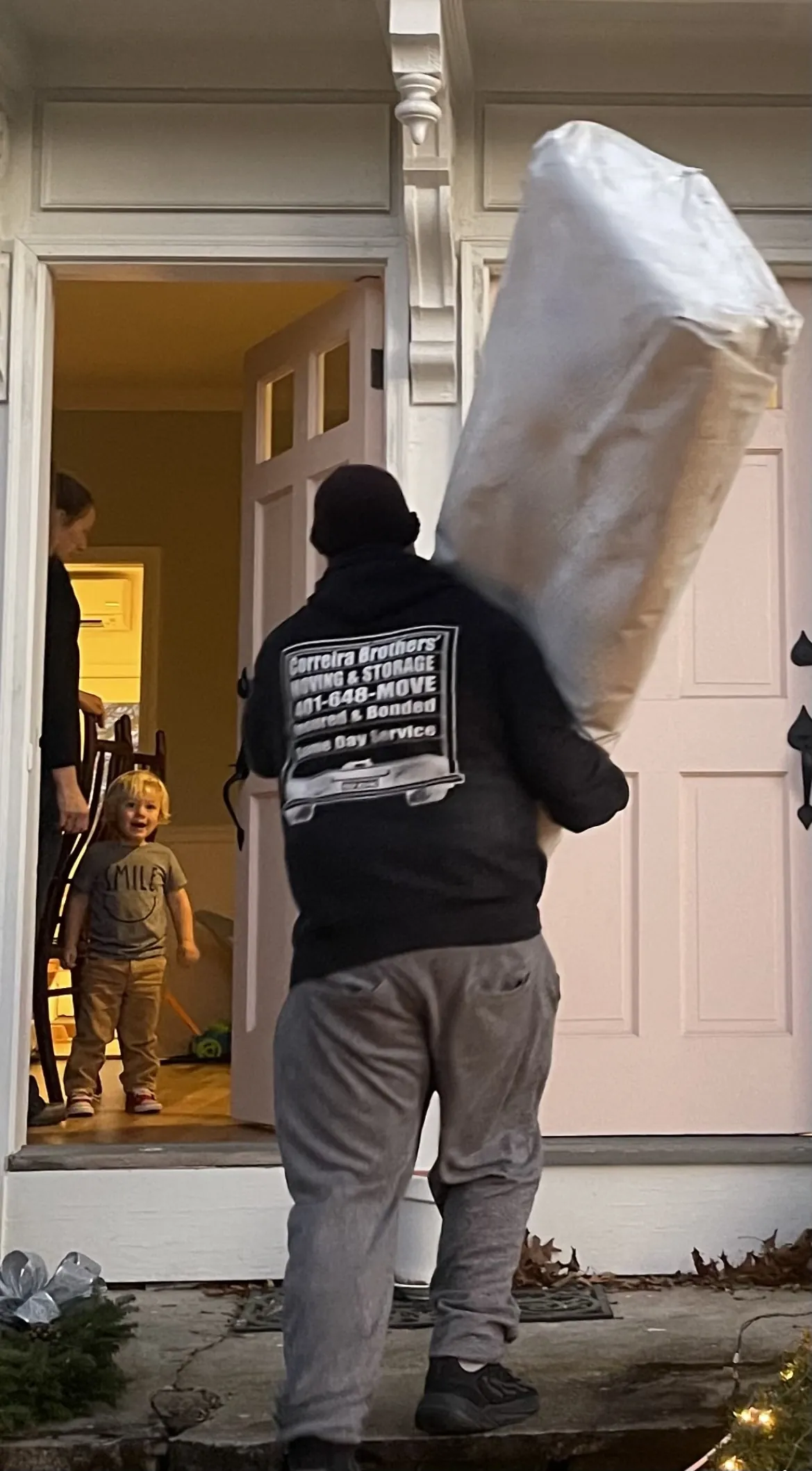 Correira Brothers mover in company hoodie carrying a wrapped item through a doorway