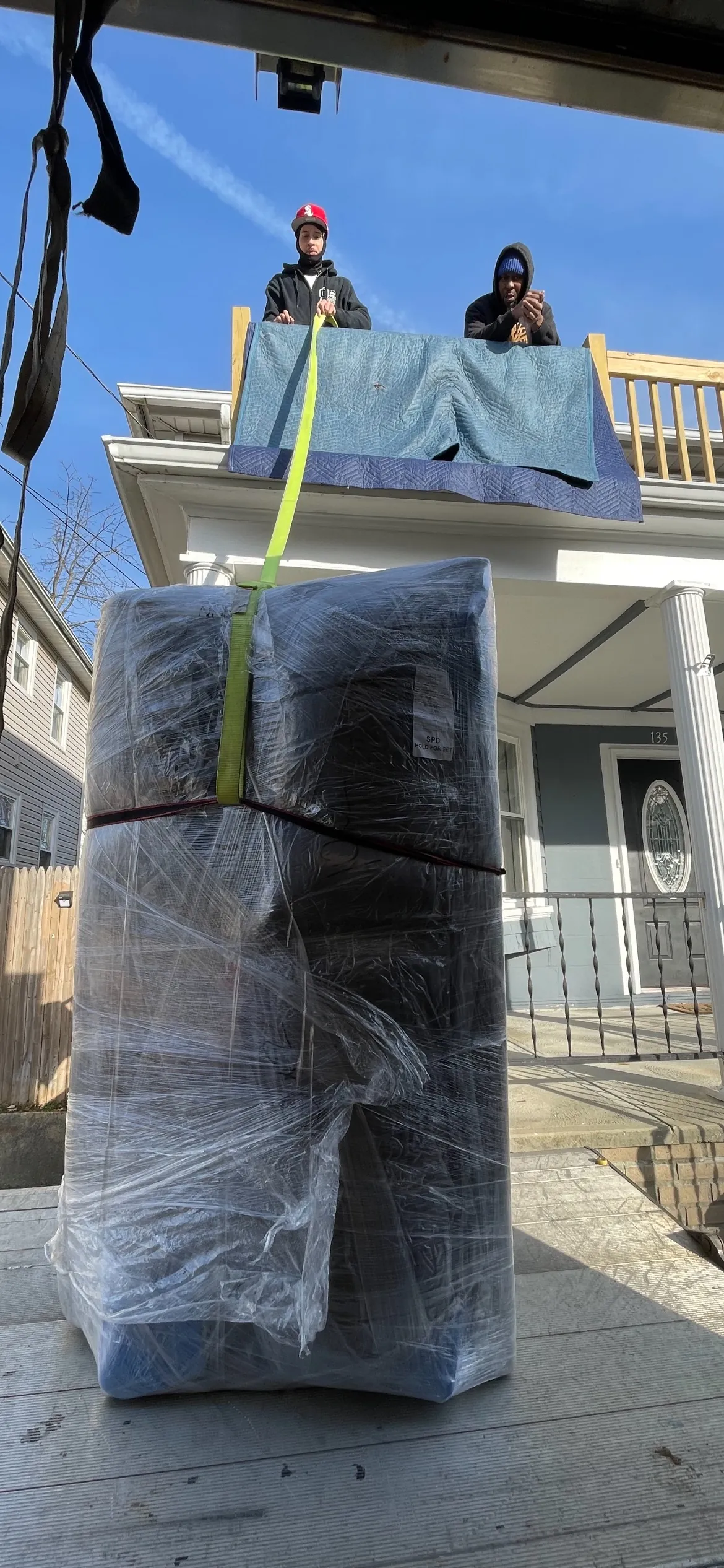 Furniture wrapped in moving blankets and strapped on a porch railing