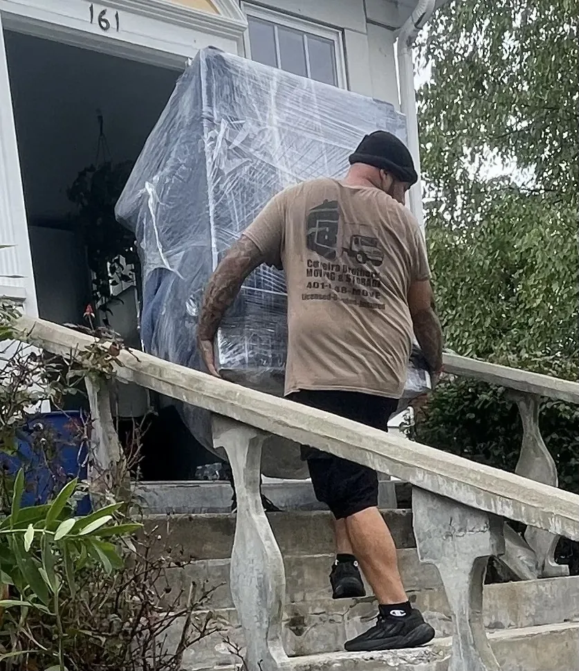 Mover carrying a shrink-wrapped item up a truck ramp outdoors