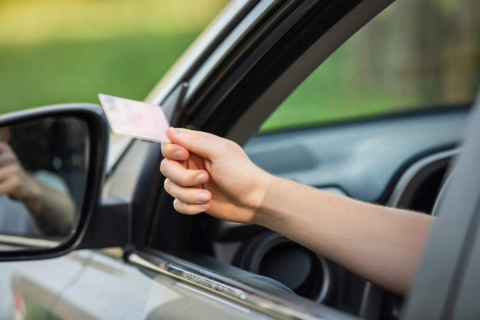 Close-up of a hand holding a driver's license out of a car window